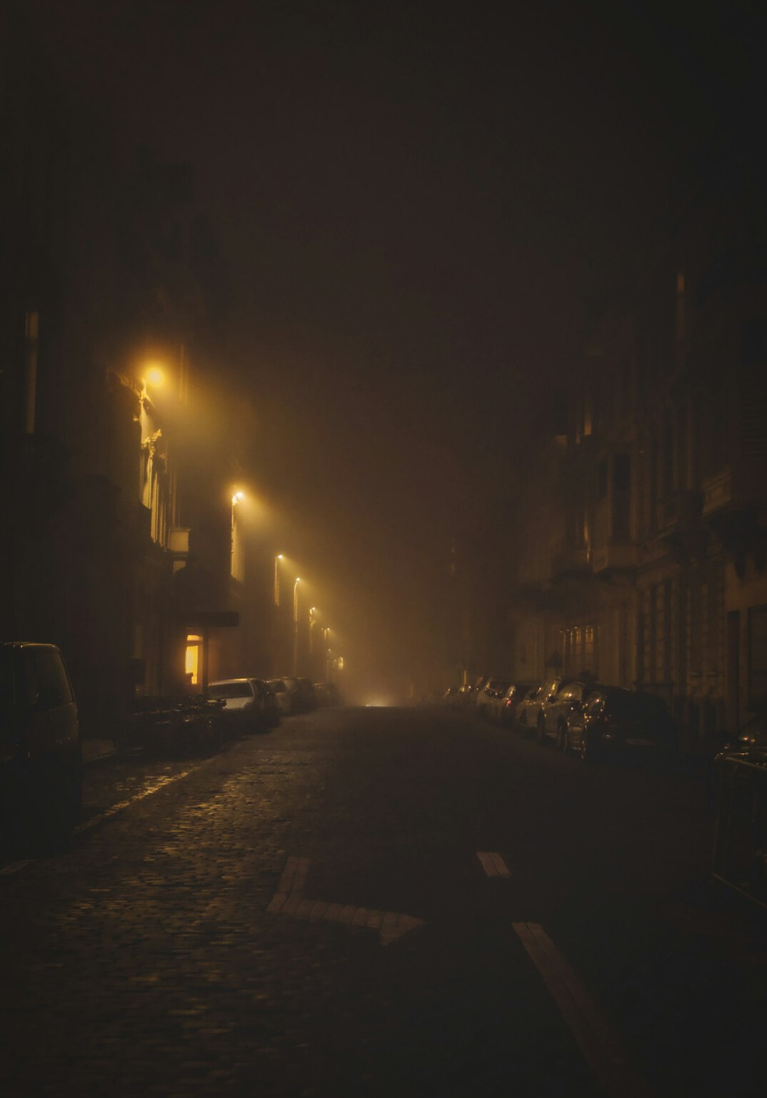 Foggy old European city street at night lit by a single streetlamp