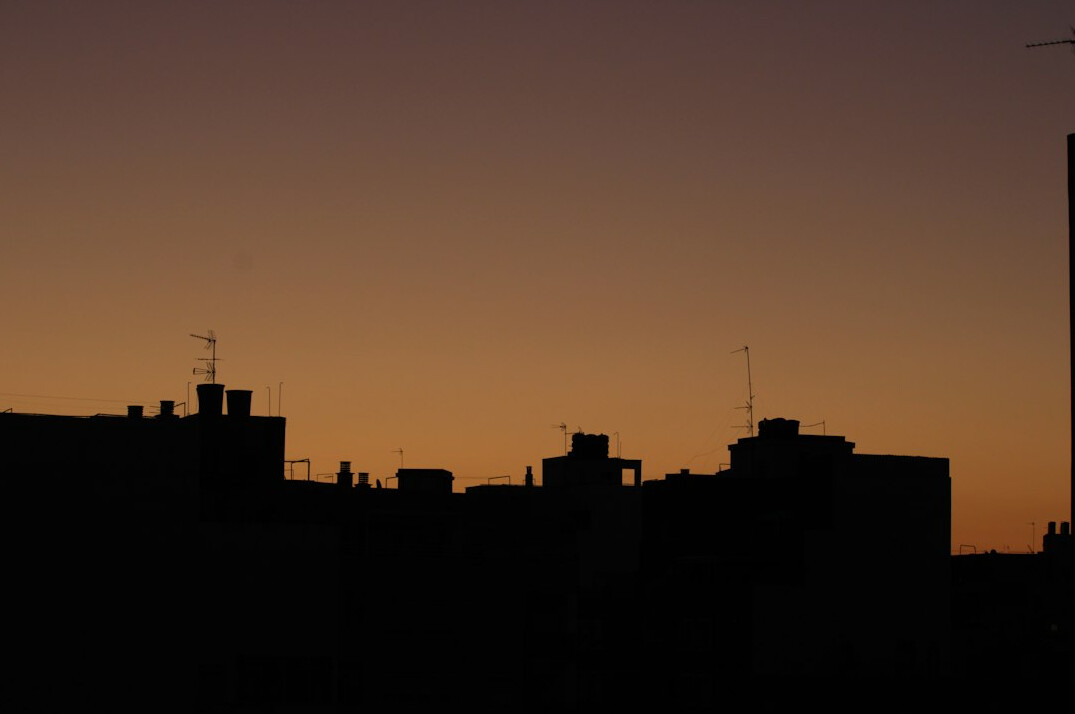 Silhouette of city rooftops against a dark dusk sky